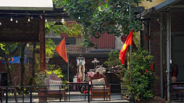 Authentic street view of a traditional Vietnamese village, featuring a patriotic Vietnamese flag waving proudly in the gentle wind.