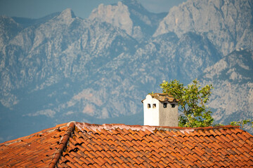 Obraz premium Traditional red tiled roof and chimney against majestic Taurus mountains in Antalya Turkey