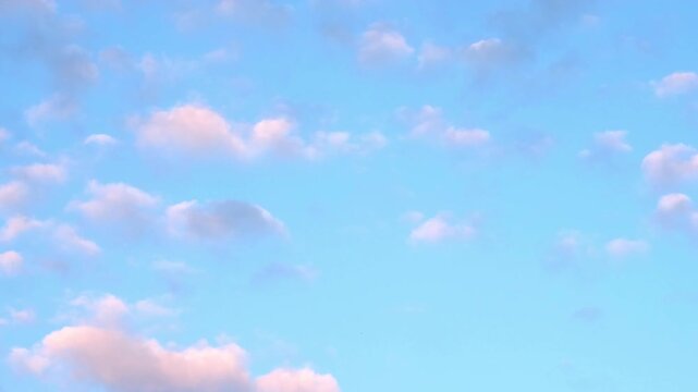 Blue sky and small pink clouds background. Sunset begins in the evening