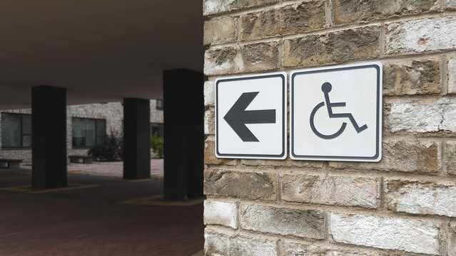 Accessible entrance direction sign with wheelchair symbol mounted on brick wall near modern residential building, highlighting inclusive design, barrier free navigation, public accessibility concept