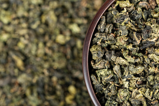 Dark wooden bowl filled with Tieguanyin on tea texture background