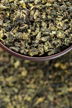 Dark wooden bowl filled with Tieguanyin on tea texture background