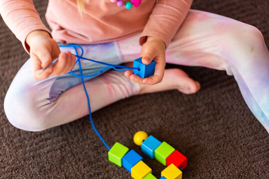 preschooler doing beading threading activity with thread and wood bead
