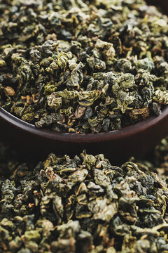 Wooden cup full of green oolong surrounded by loose tea texture