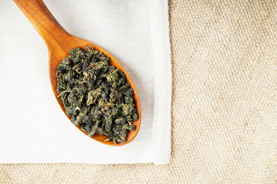 Top view closeup rustic spoon filled with loose tea on craft fabric