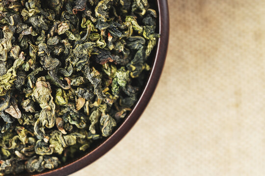 Overhead macro of green oolong in wooden cup on light burlap
