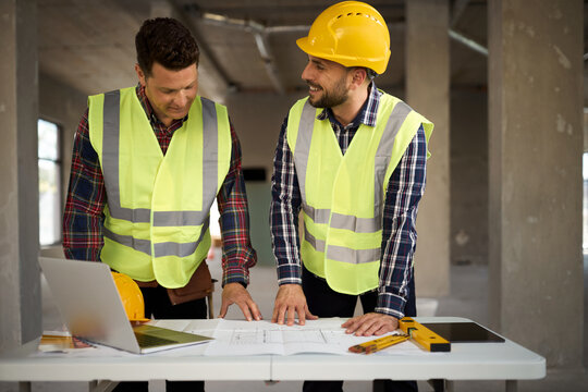 Happy workers cooperating while reading plans  at construction site