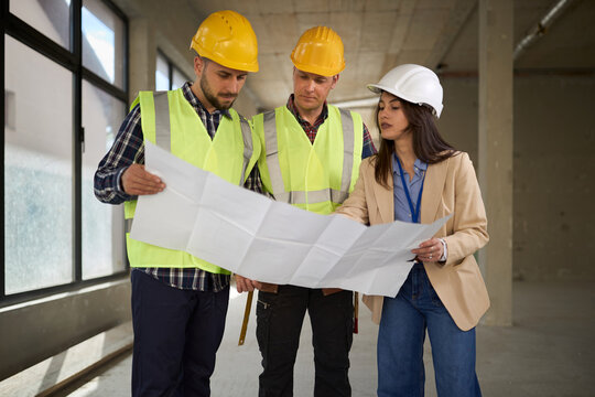 Female project manager and  workers working on plans at construction site.