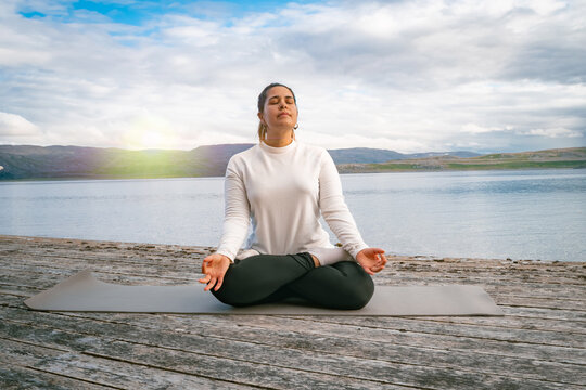 Woman meditating in lotus positionon a wooden pier by a scenic fjord in Norway