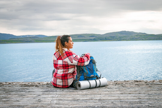 Female backpacker sitting on a wooden pier with heavy rucksack looking at the fjord in Norway