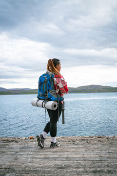 Female backpacker with heavy rucksack walking on a wooden by a fjord in Norway