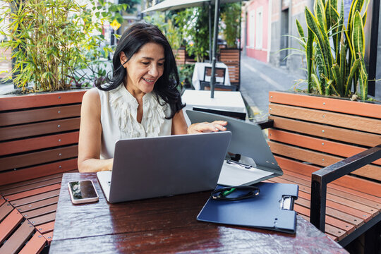 senior latin woman using laptop and having fun outdoors in terrace in Mexico Latin America, mexican female working with computer  