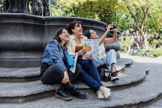 senior women latinas friends traveling and holding a tourist map in Mexico downtown in Latin America, hispanic middle age people tourist in fountain in colonial city 