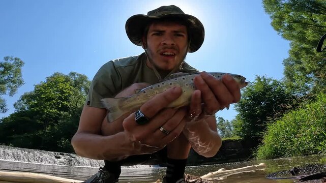 Young angler holding and releasing a caught Brown Trout (Salmo trutta) back into a river. Summer catch and release conservation concept.