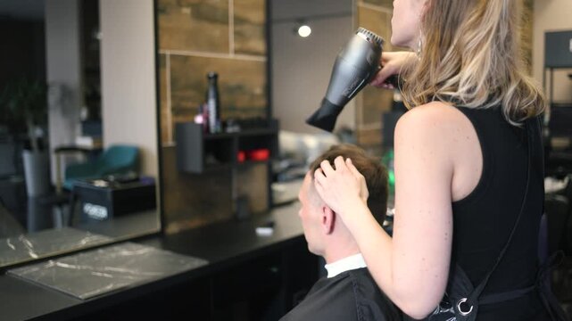 A skilled barber focuses intently as he uses clippers to shape a man's fresh haircut in a lively salon setting filled with the sounds of chatter and buzzing tools in the afternoon light.