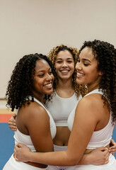 Obraz premium Three smiling cheerleaders embracing indoors