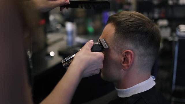 A skilled barber focuses intently as he uses clippers to shape a man's fresh haircut in a lively salon setting filled with the sounds of chatter and buzzing tools in the afternoon light.