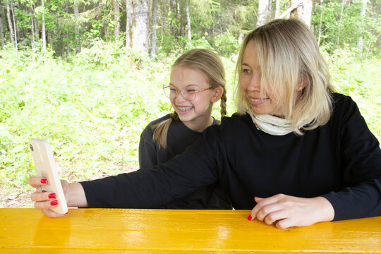 A mother and daughter are taking selfies in the forest in the summer.