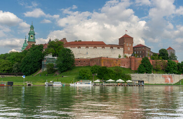 Panoramic view of Wawel Royal Castle overlooking the Vistula River in Krakow, Poland. Medieval fortifications, cathedral towers, riverside promenades, and calm water reflections capture one of the cou © Volha