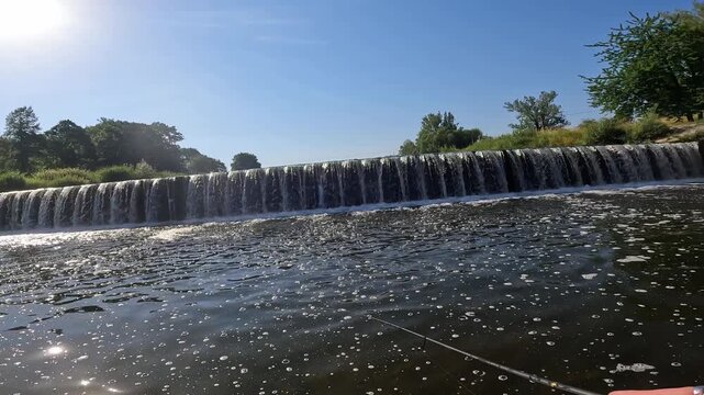 POV catching a wild European Chub (Squalius cephalus) near a sunny river weir using a spinning rod and landing net.