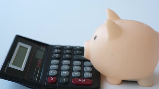 Hand putting coins into piggy bank next to calculator on white table. investment and insurance concept