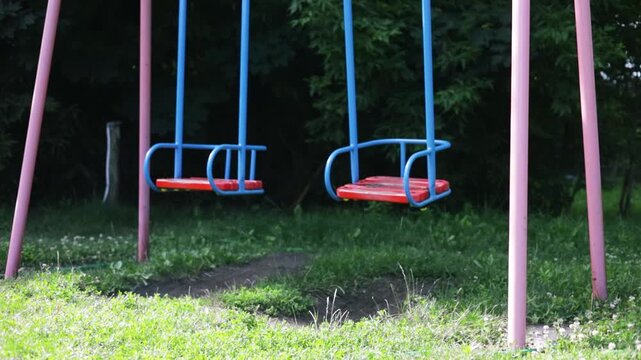 Empty swing seat gently moving on a peaceful green playground