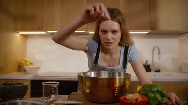Woman in the kitchen learning to cook. Leaning close to the bowl and seasoning the food. Following the recipe instructions to make a vegan salad