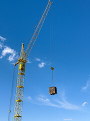 Naklejka premium Yellow tower crane lifting heavy load against blue sky