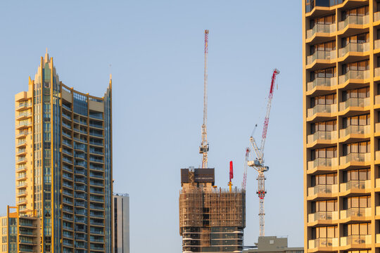 Modern skyscrapers and construction cranes against a clear blue sky at sunset