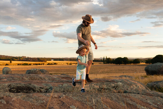 Father and young daughter on adventure over rocks through grassy paddock at sunset
