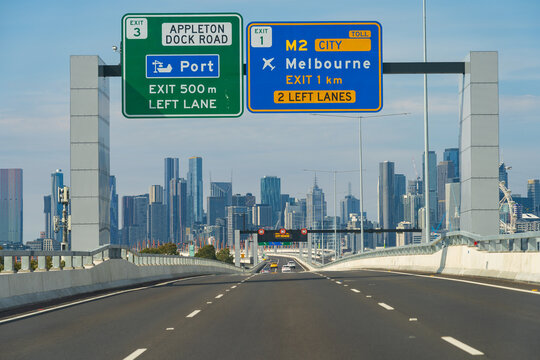 View along a multi-laned freeway with overhead signage toward a city skyline