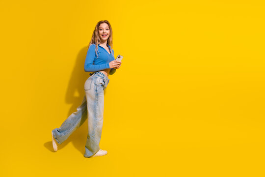 Young stylish woman smiling and holding a smartphone on a vibrant yellow background to promote modern lifestyle and fashion