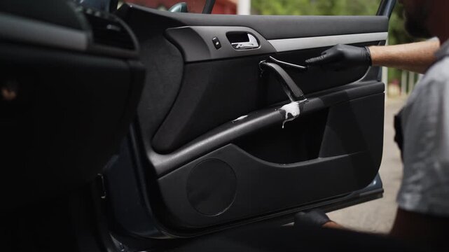 Close-up view of a professional auto detailer's hands in protective gloves meticulously cleaning the plastic interior door panel with a special foam chemical and a brush