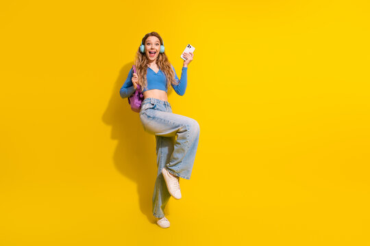 Joyful young woman with backpack smiling confidently against bright yellow backdrop, showcasing positivity and energy