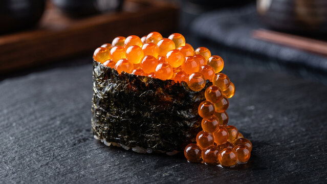 Glistening ikura gunkan maki sushi overflowing with bright orange salmon roe on a dark slate platter