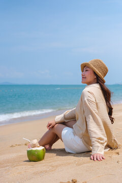 Vertical portrait image of a woman enjoy sitting with a fresh coconut juice on the beach