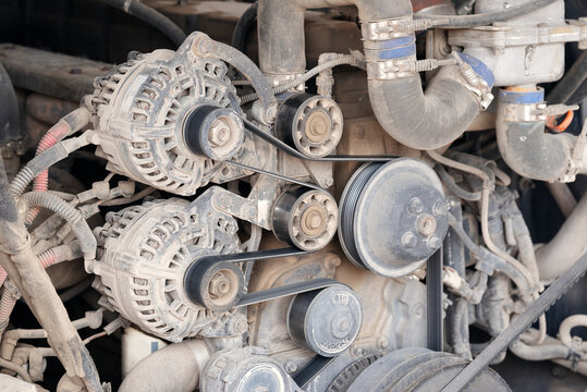 Focused view on two heavy-duty alternators driven by multi-groove serpentine belts with tensioner and idler pulleys on a large diesel engine.