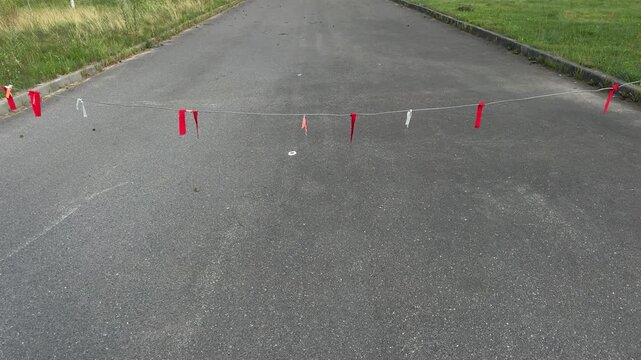 Rope with red and white flags stretched across asphalt road blocking passage, outdoor barrier marking