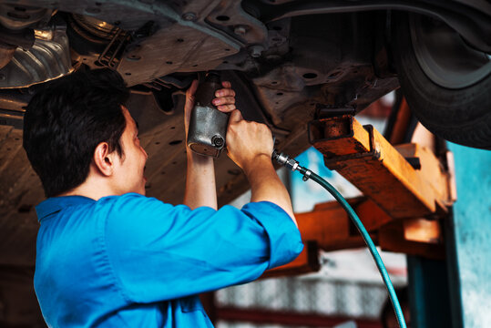 Car Repair Performed with a Pneumatic Impact Wrench as an Auto Mechanic Works Beneath a Raised Vehicle Inside an Automotive Service Garage During Routine Maintenance