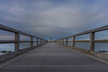 Obraz premium Low angle perspective of wooden pier boardwalk extending into calm ocean under clouds