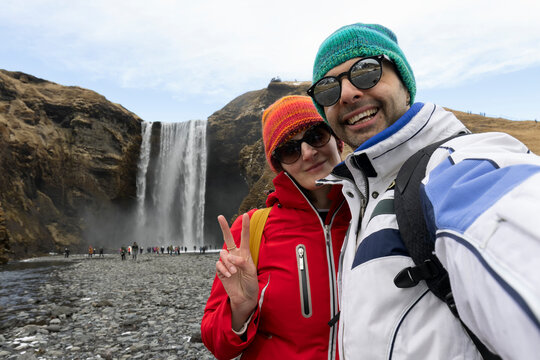 Smiling couple, man and woman making selfie on a Skogafoss waterfall background, Iceland.