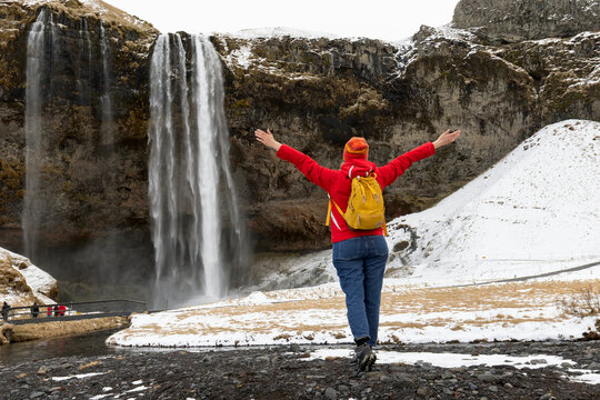 Woman in red with arms raised on the Seljalandsfoss waterfall, Iceland