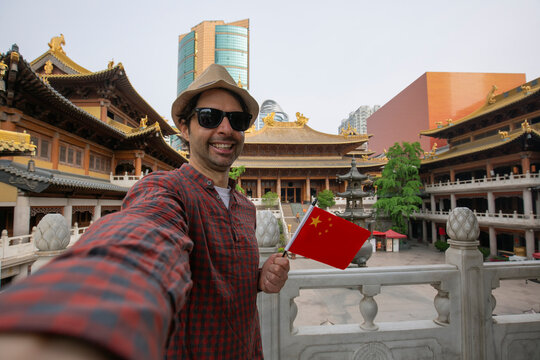 Happy  tourist taking a fun selfie with chinese's flag at the famous tourist attraction in China. Asia summer travel. Young man taking mobile picture with smartphone at Temple.