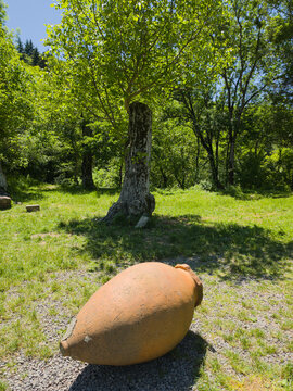 Traditional Georgian clay qvevri wine vessel lying on ground in monastery garden under sunny green trees in Shida Kartli, Georgia
