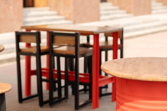 Empty outdoor street cafe furniture setup with industrial loft style wooden tables and high metal bar stools.