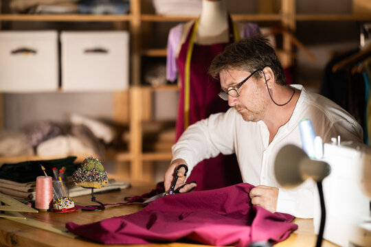 Middle-aged male dressmaker cutting textile in sewing workshop