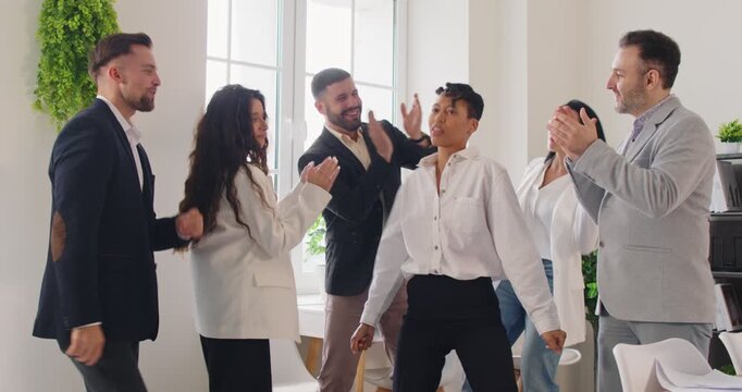 Young funny happy business people and employees in suits having fun and dancing celebrating success in business or making a deal in office. Teamwork and teambuilding concept. 4k video. Slow motion