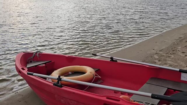 Red rescue boat with oar and lifebuoy moored on a sandy shore.