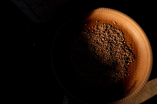 Top-down view of raw parchment coffee beans in a traditional woven winnowing tray under dramatic lighting.