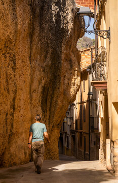 A man is walking through the streets of Margalef among houses and rocks.